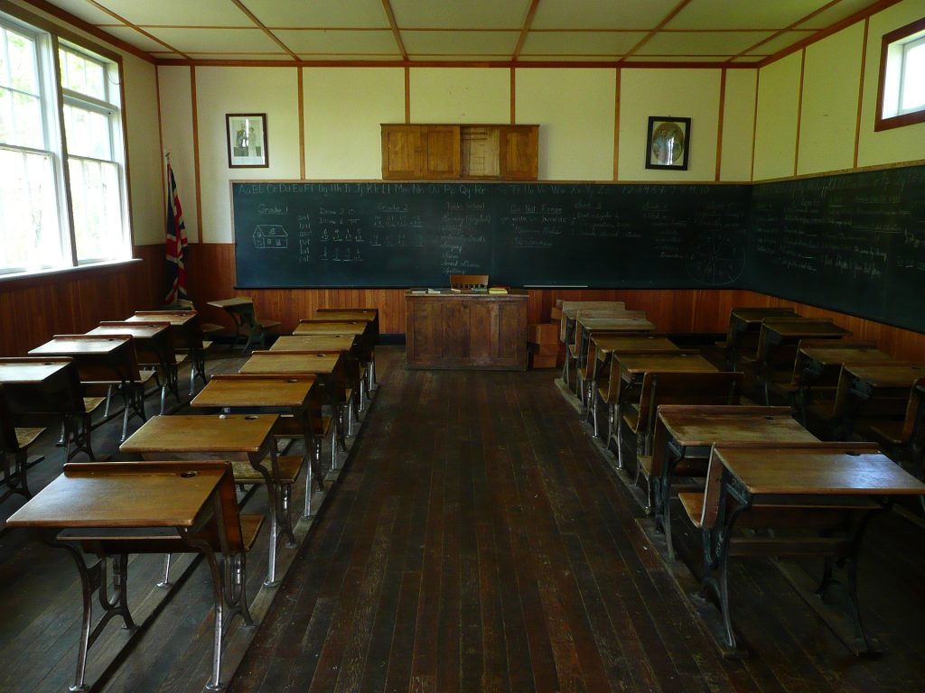 Cette image est l'illustration d'une salle de classe avec les tables en bois et le tableau à craie